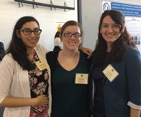 Three smiling graduate students with name tags at a conference.